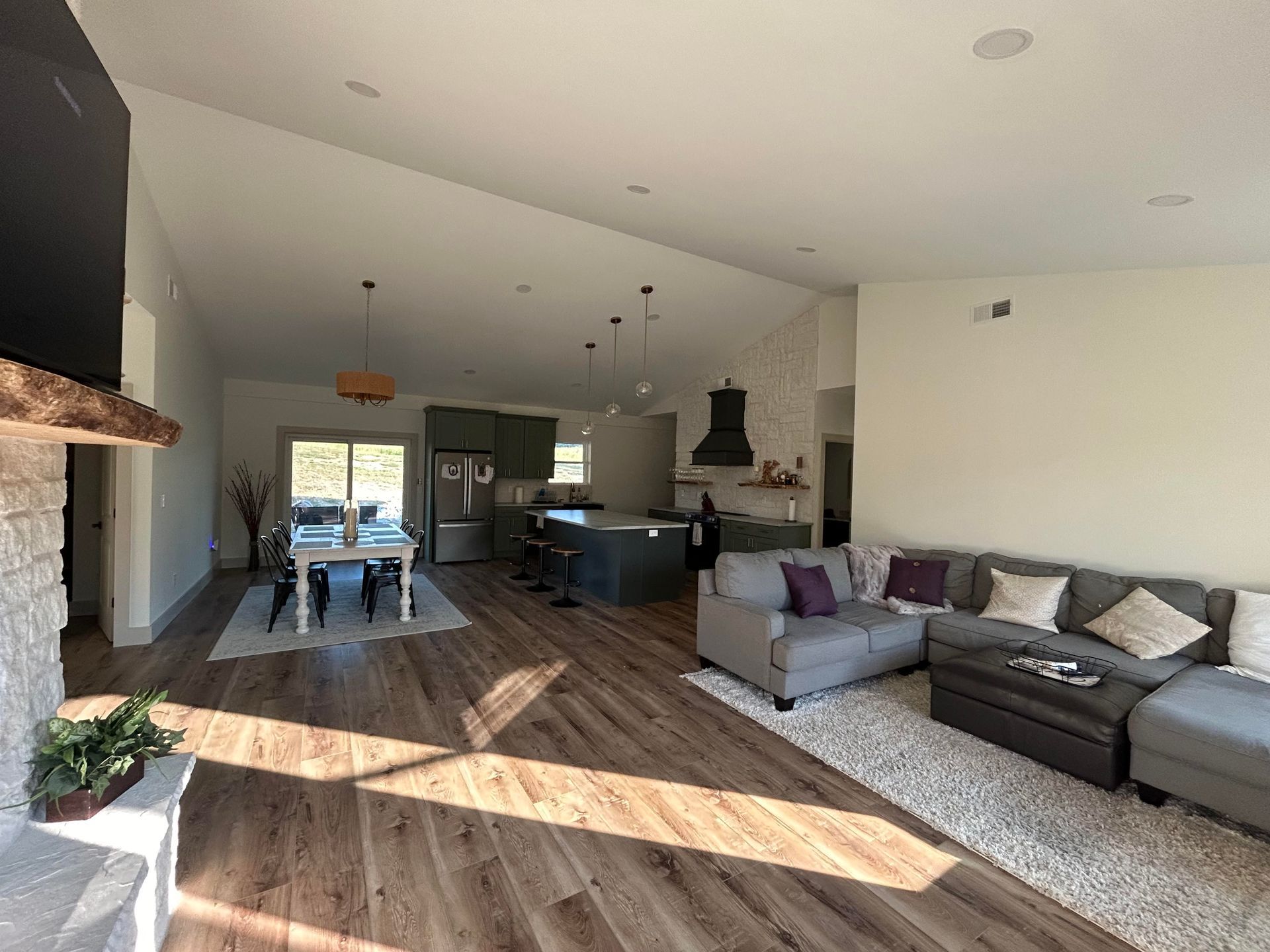 An open-concept living area with wood floors, a gray sectional, and a kitchen featuring a dark island and dining table.
