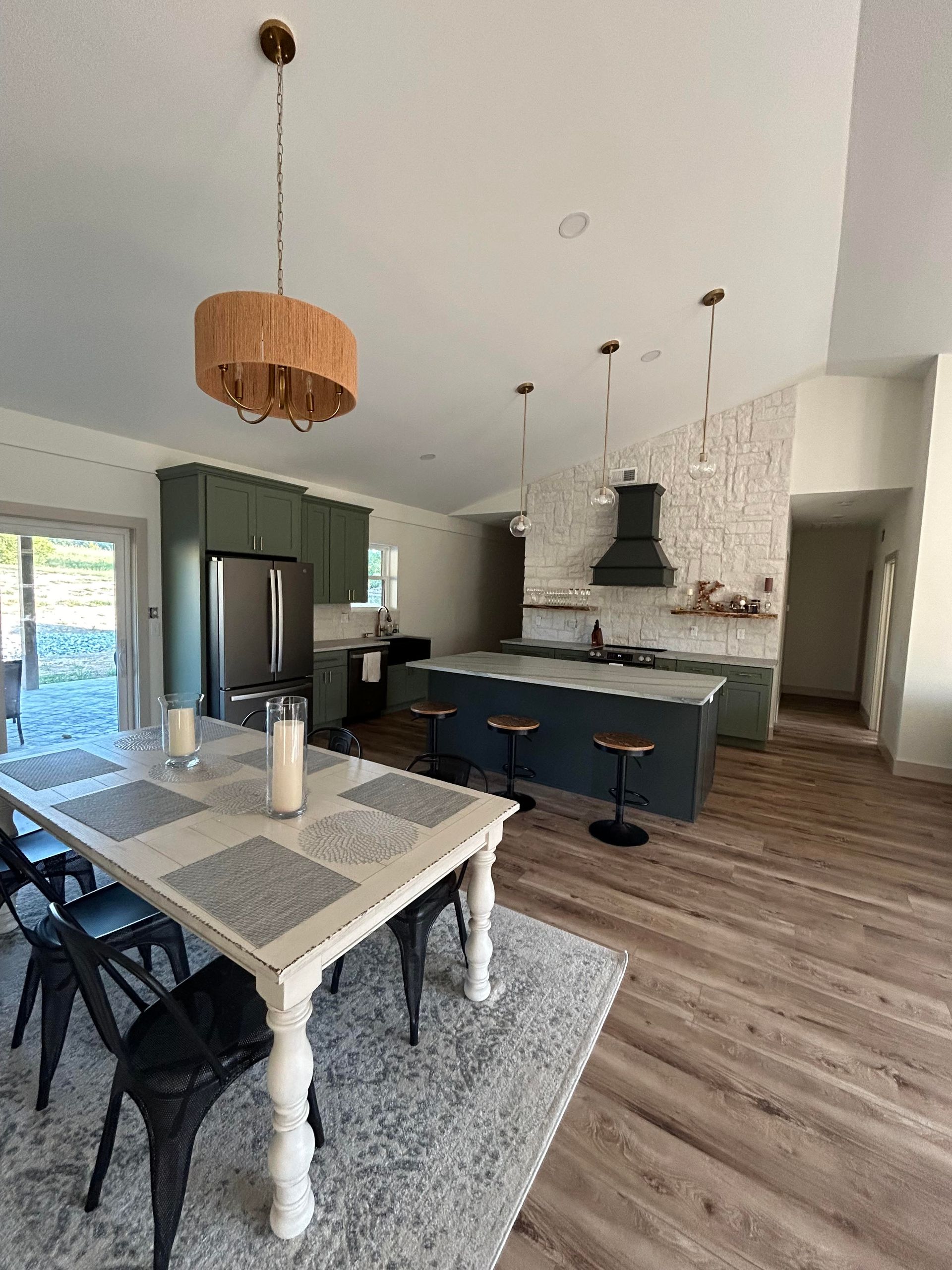 Modern kitchen with a light-colored dining table, gray area rug, kitchen island with bar stools, and stone accent wall.