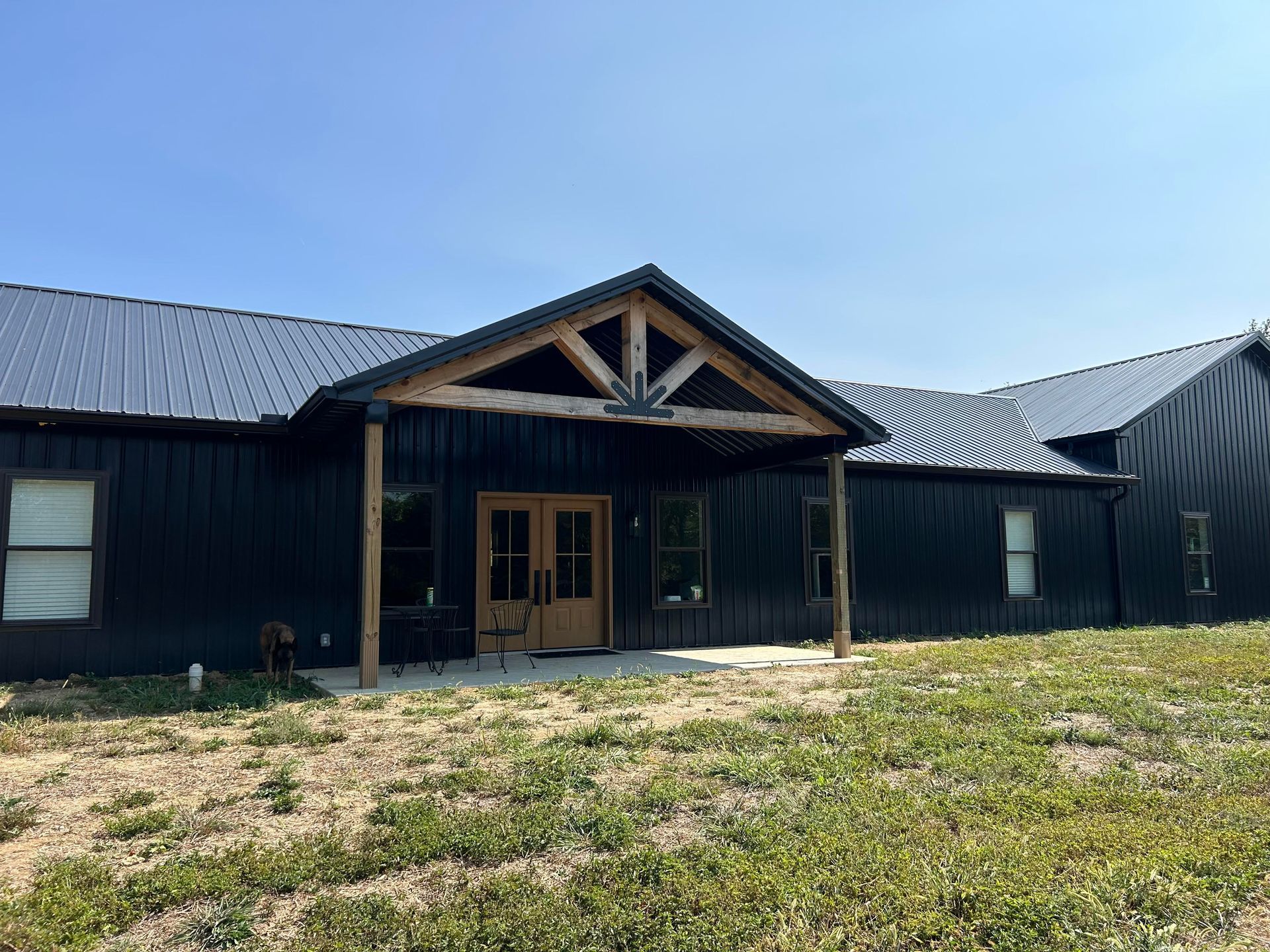 A modern black metal-sided building with a wooden gable porch entrance, set against a bright blue sky.