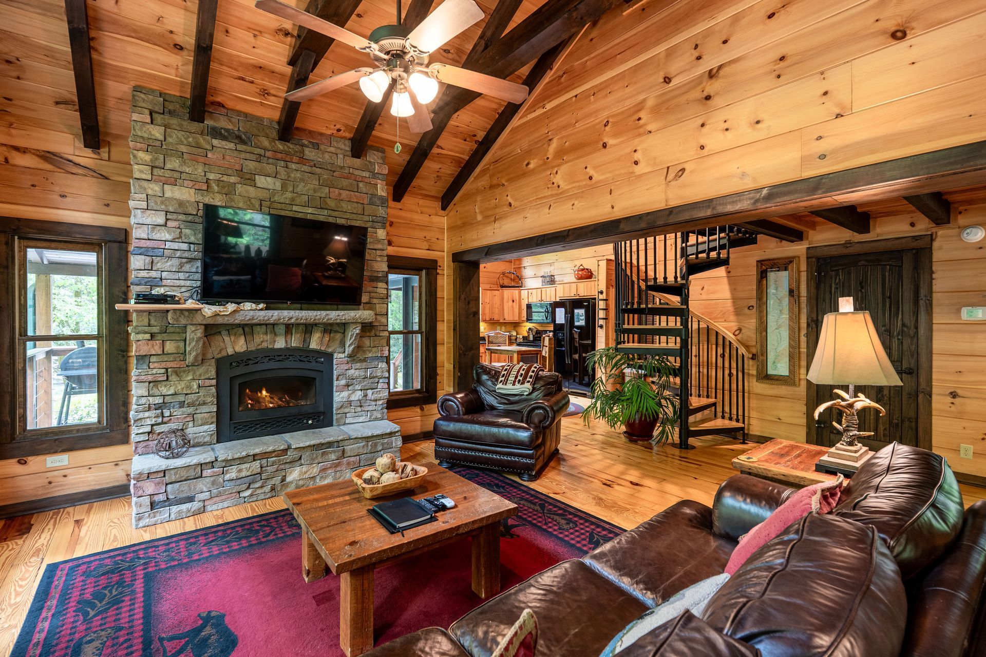 Cozy cabin living room with fireplace, leather furniture, and spiral staircase.