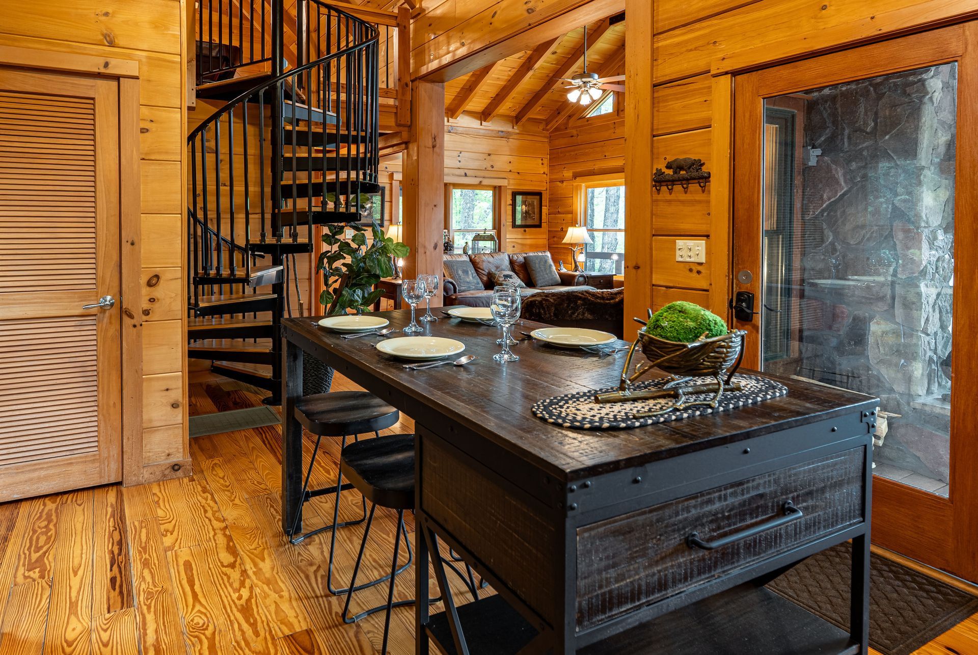 Rustic cabin interior with dark wood kitchen island, spiral staircase, and open living area.