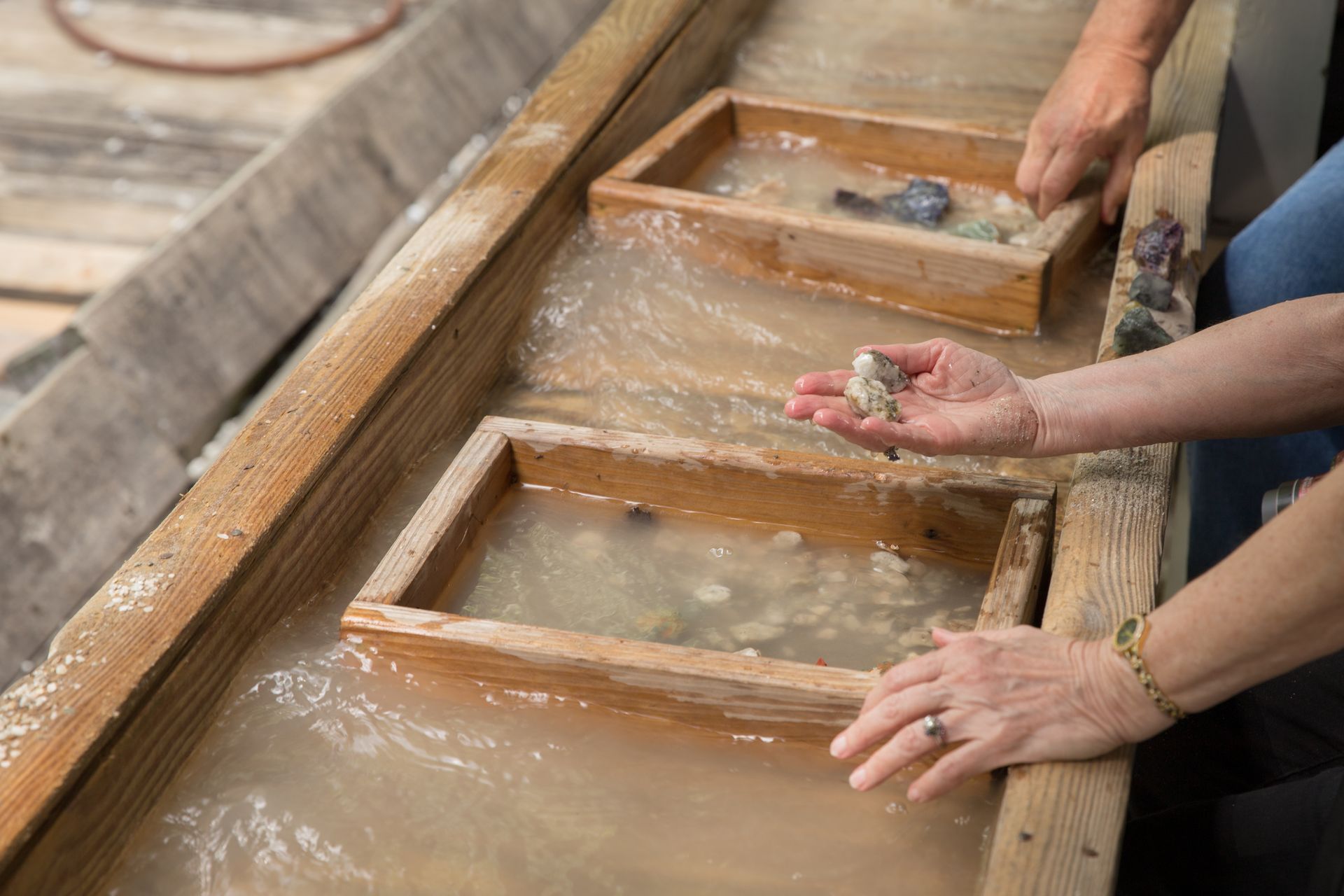 Hands sifting through trays of water, searching for gems at a gem mining experience.