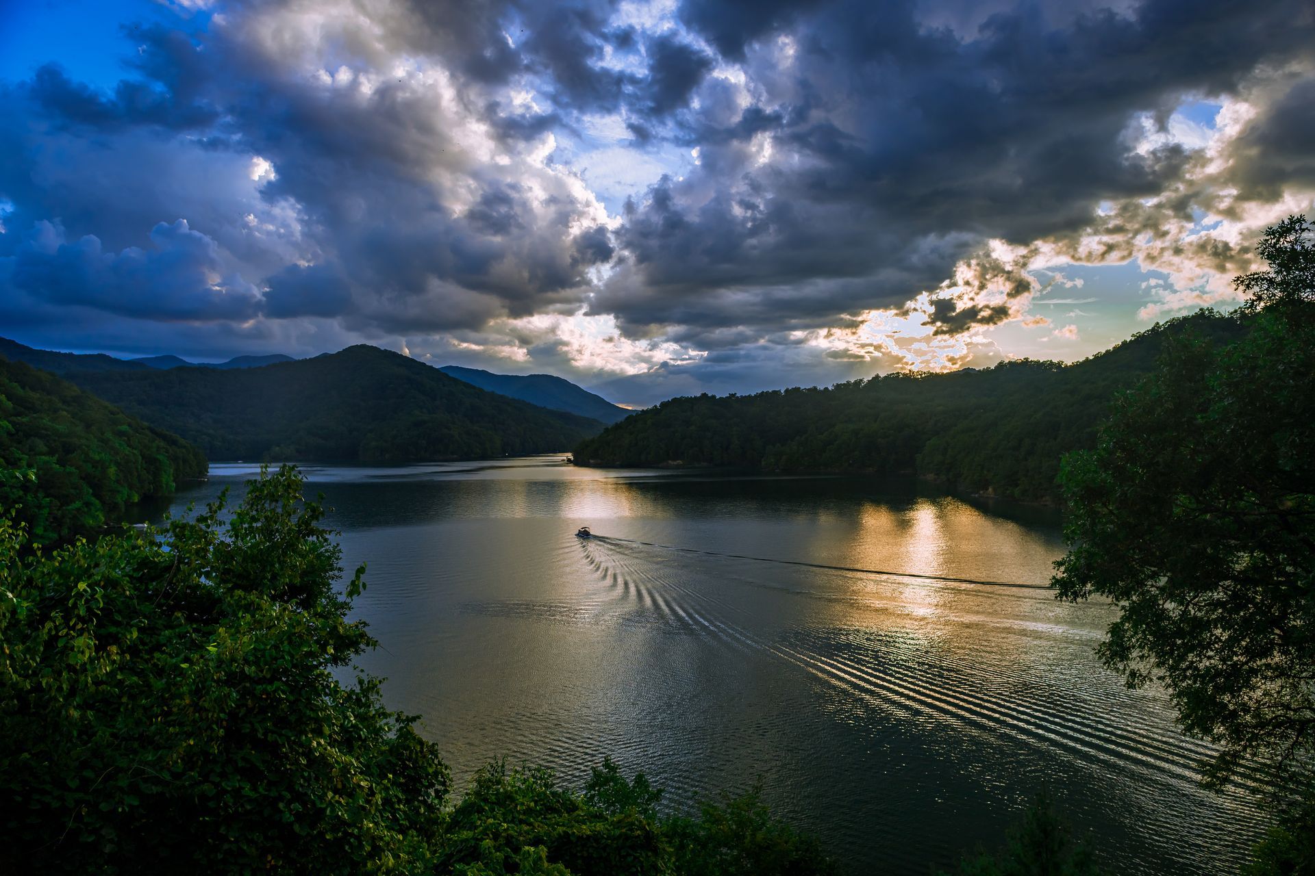 Dramatic lake scene with dark clouds, mountains, and a boat. Sun breaks through the clouds.