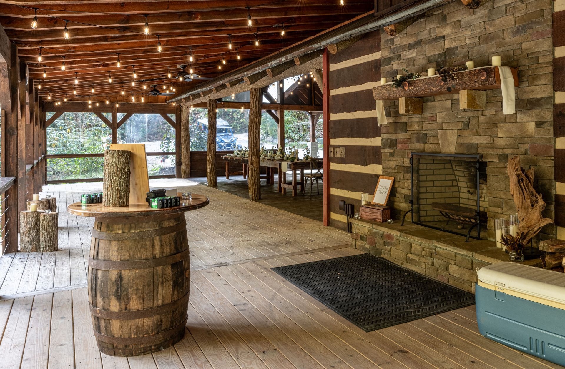Covered patio with a stone fireplace, bar, wooden beams, and string lights.