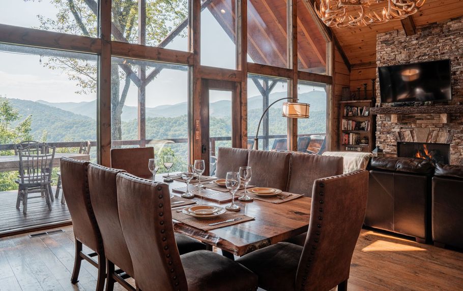 Lodge interior with a leather sectional, large windows overlooking a deck, and dining area with a pool table.