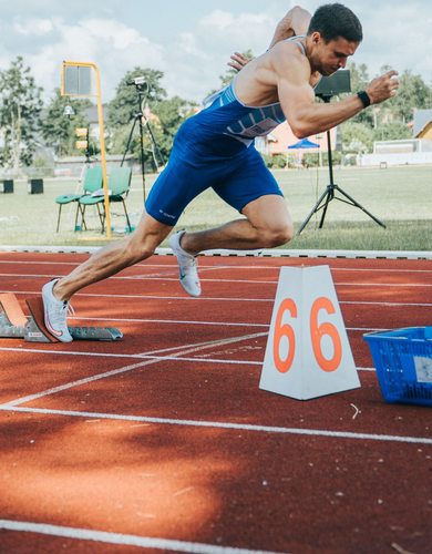 Sprinter in blue racing gear launching from starting blocks on a track, lane 66 visible