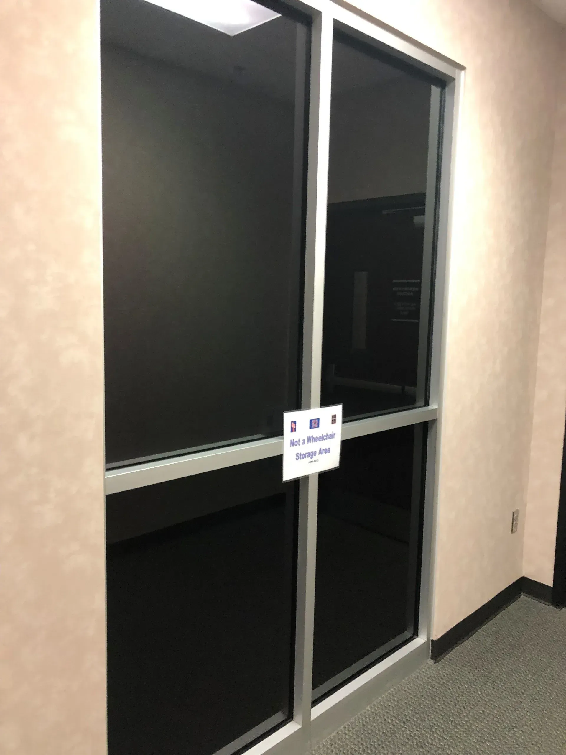 Dark glass double doors with a small sign, in a beige hallway.