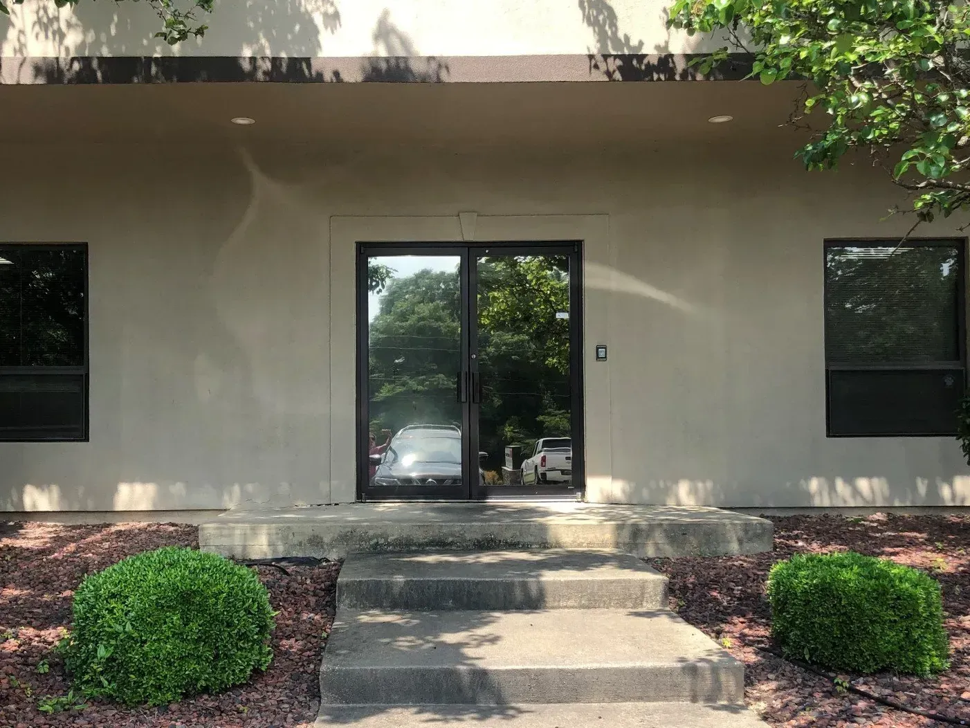 Building entrance with glass double doors, steps, and trimmed bushes in front