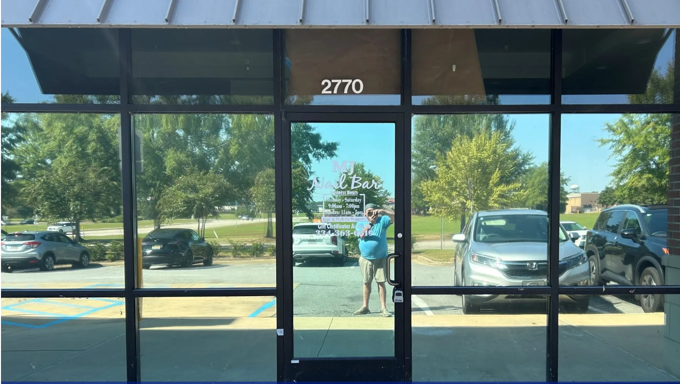 Storefront glass entrance with number 2770, reflecting parked cars and a person standing outside.