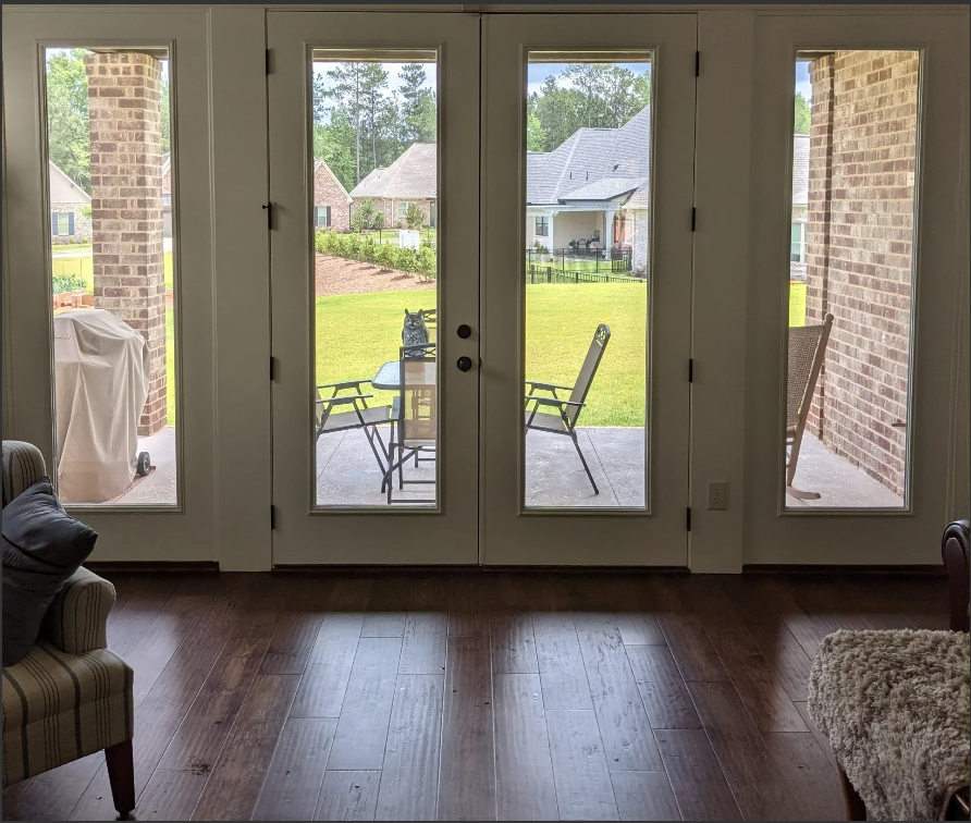 Living room view through glass doors to a backyard patio with chairs and neighboring houses