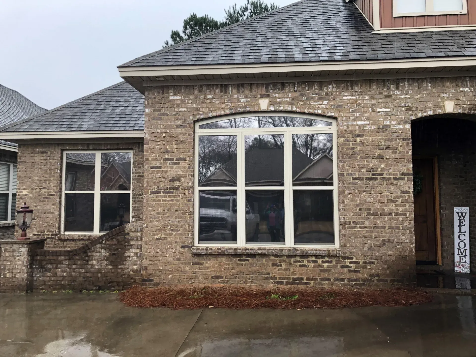 Brick house exterior with large arched window and wet driveway after rain