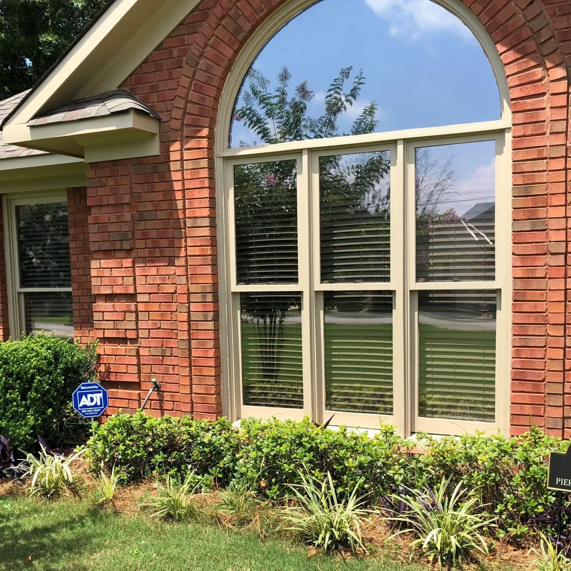 Brick house window with arched brick trim, white shutters, and shrubs in front