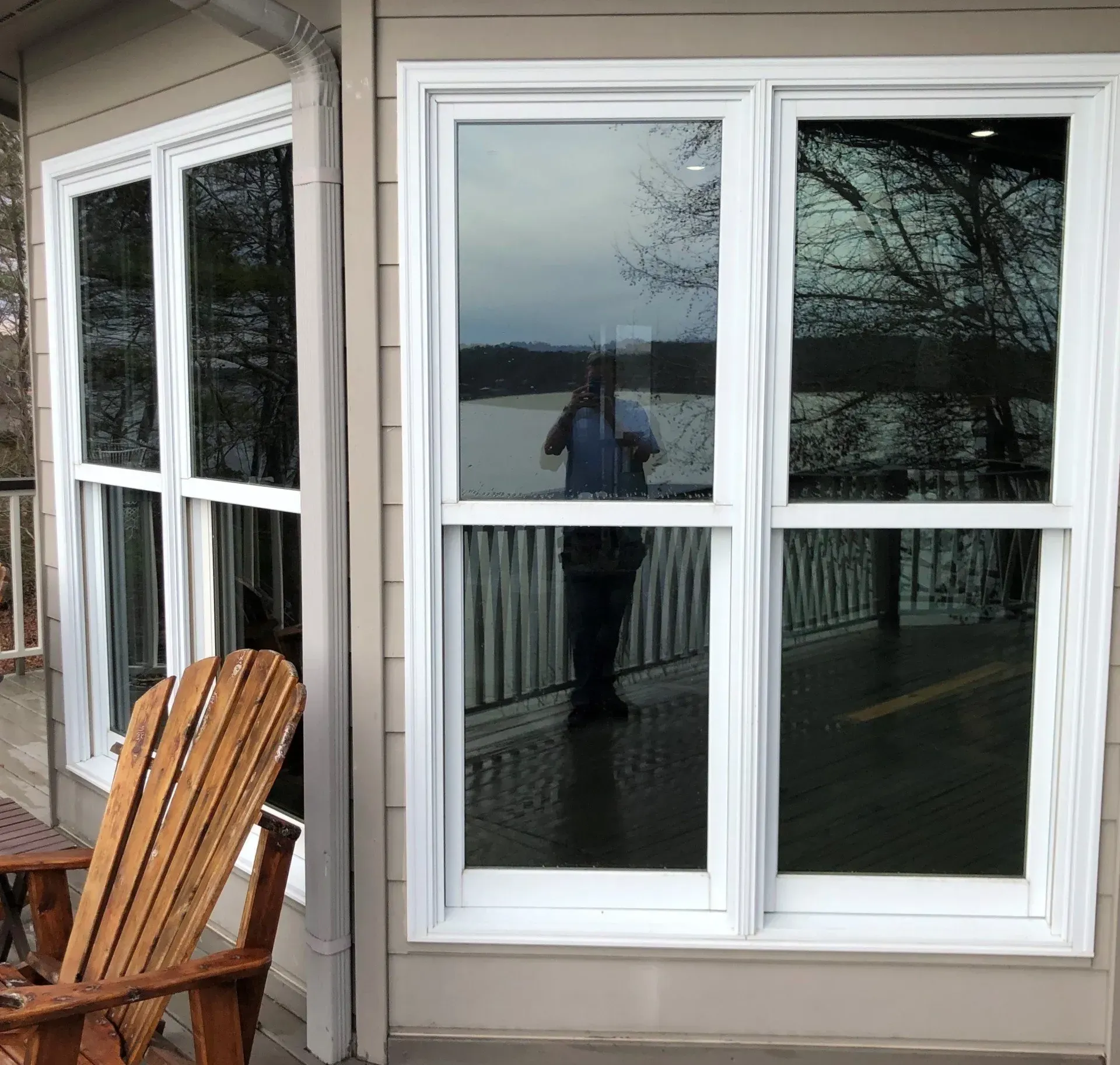 White-framed sliding glass door on a porch, reflecting trees and a person, with a wooden chair nearby