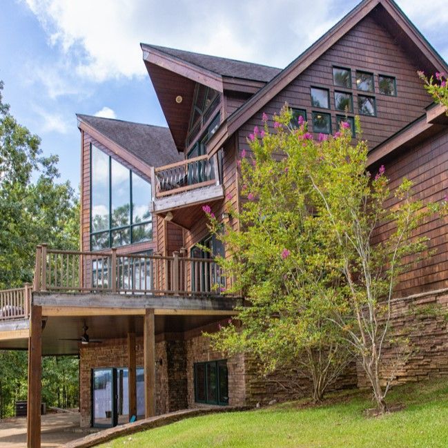 Modern rustic wooden house with large glass windows, balconies, and a covered patio on a wooded hillside