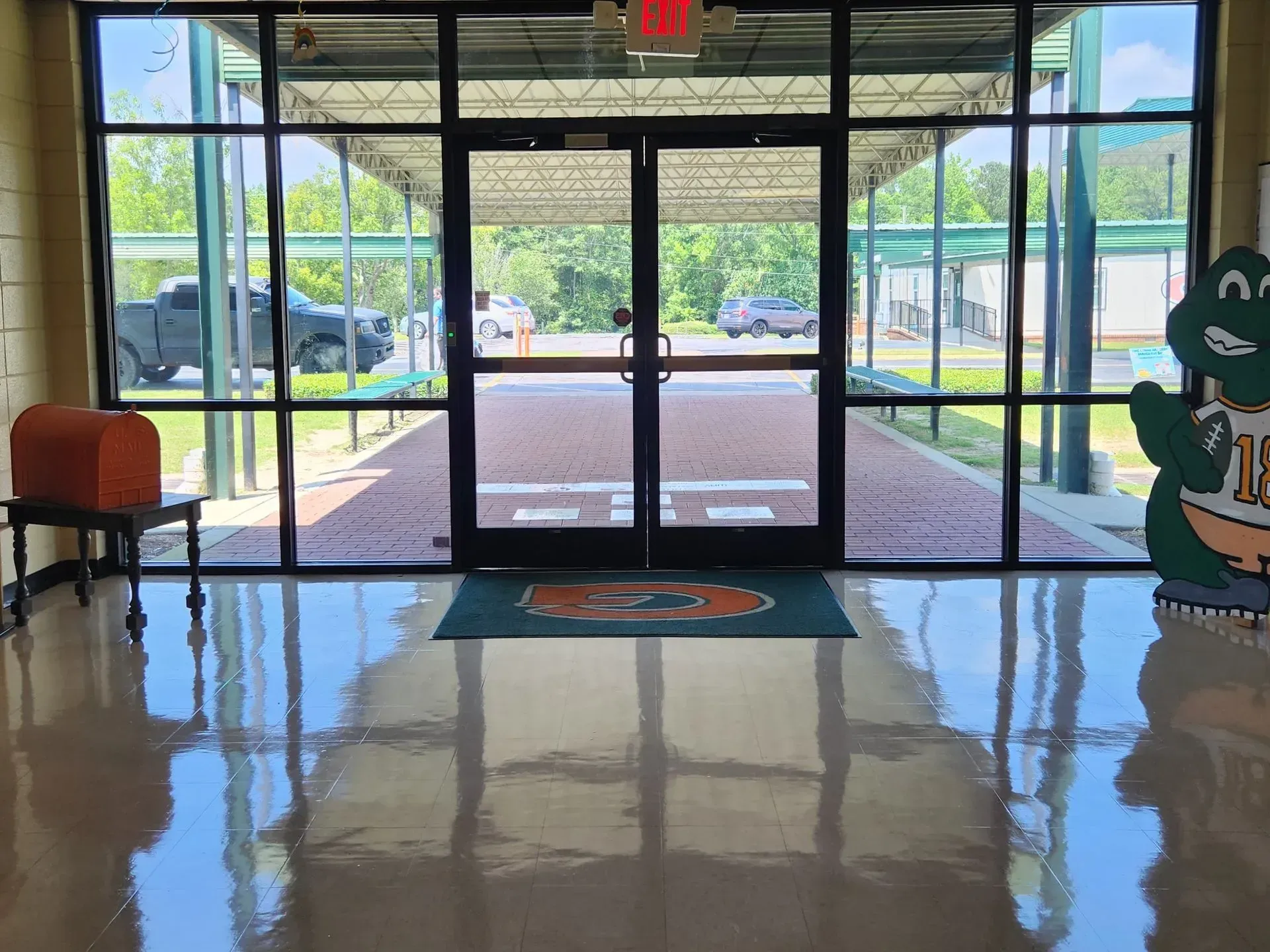 Lobby entrance with glass doors, glossy floor, and a dinosaur cutout on the right.