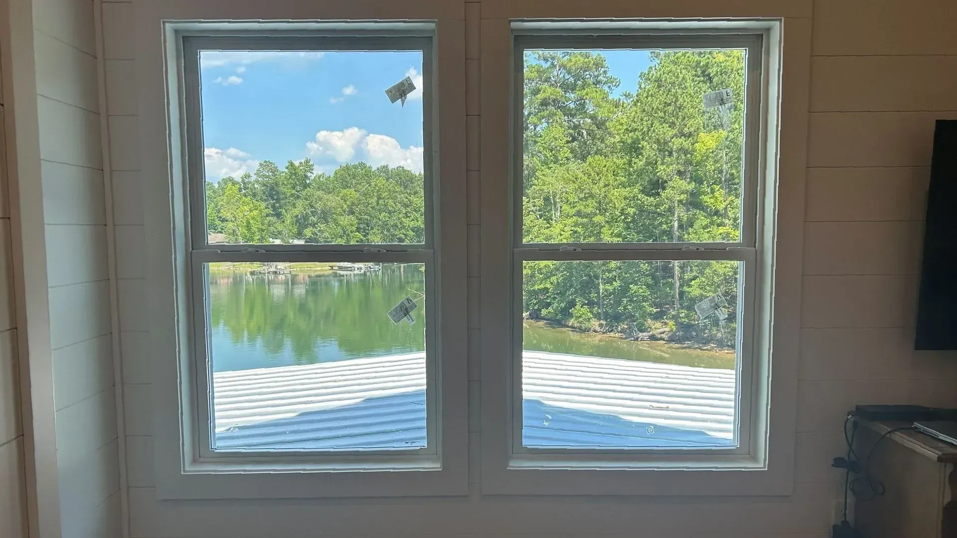 Two white-framed windows overlooking a calm lake and green trees on a sunny day