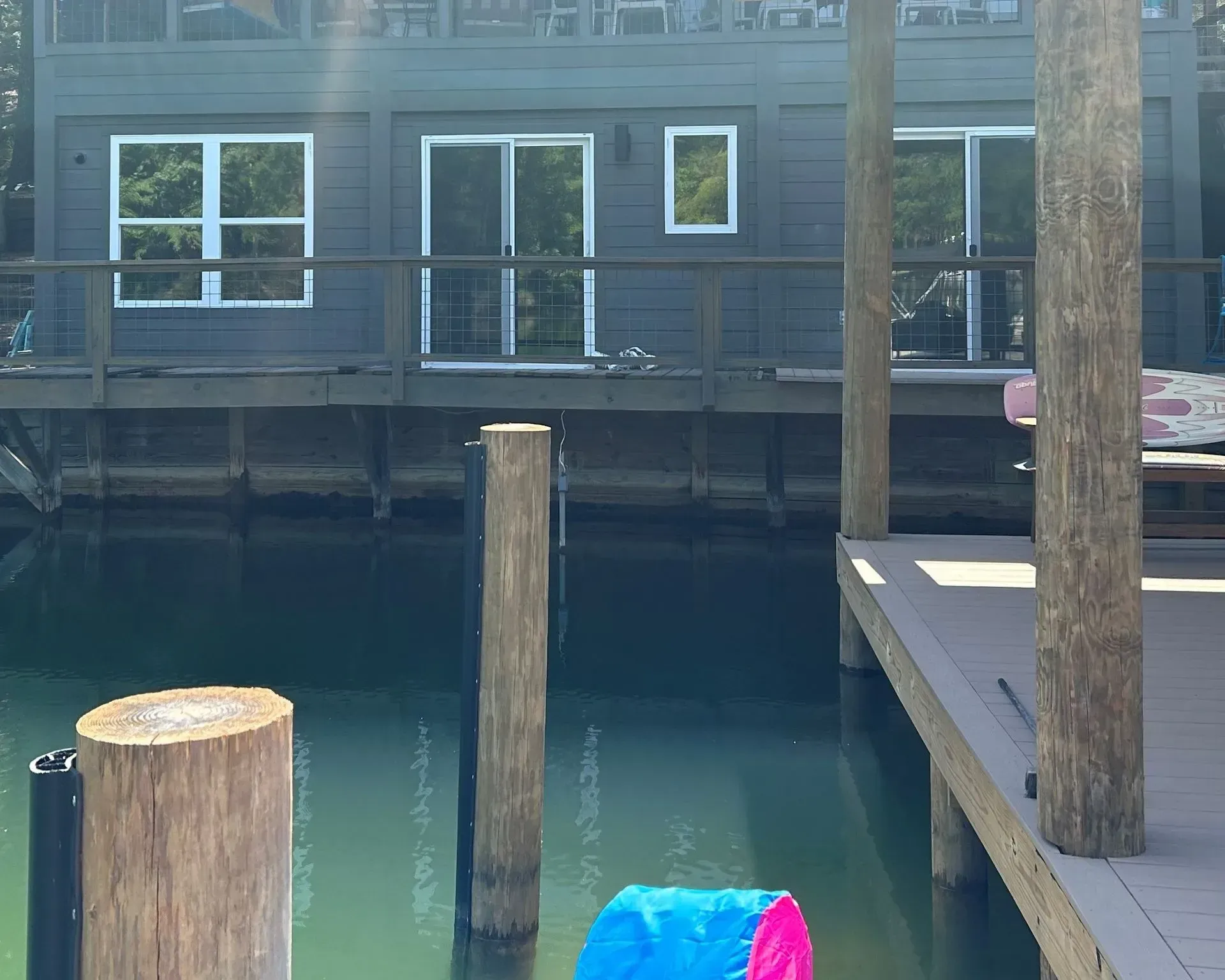Dock by calm water with dark wooden building, posts, and a small blue-pink object in the foreground