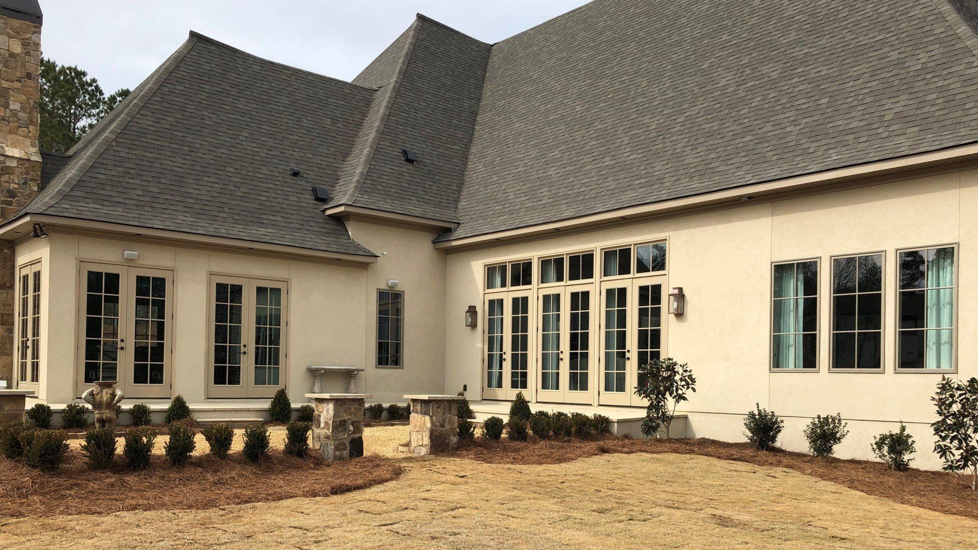 Large cream-colored house with dark gray roof, many windows, and a landscaped front yard