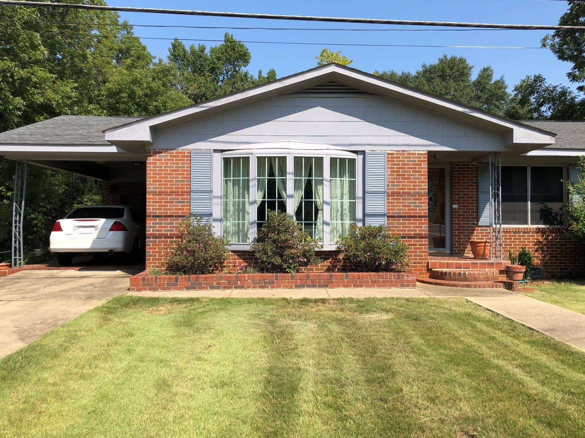 Single-story brick house with a carport, white car, and neatly trimmed front lawn