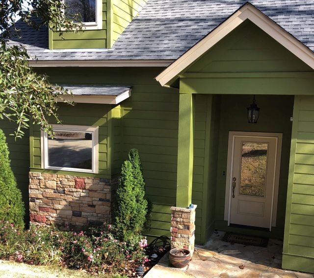 Green house entrance with stone accents, front porch, and a white door under a peaked roof