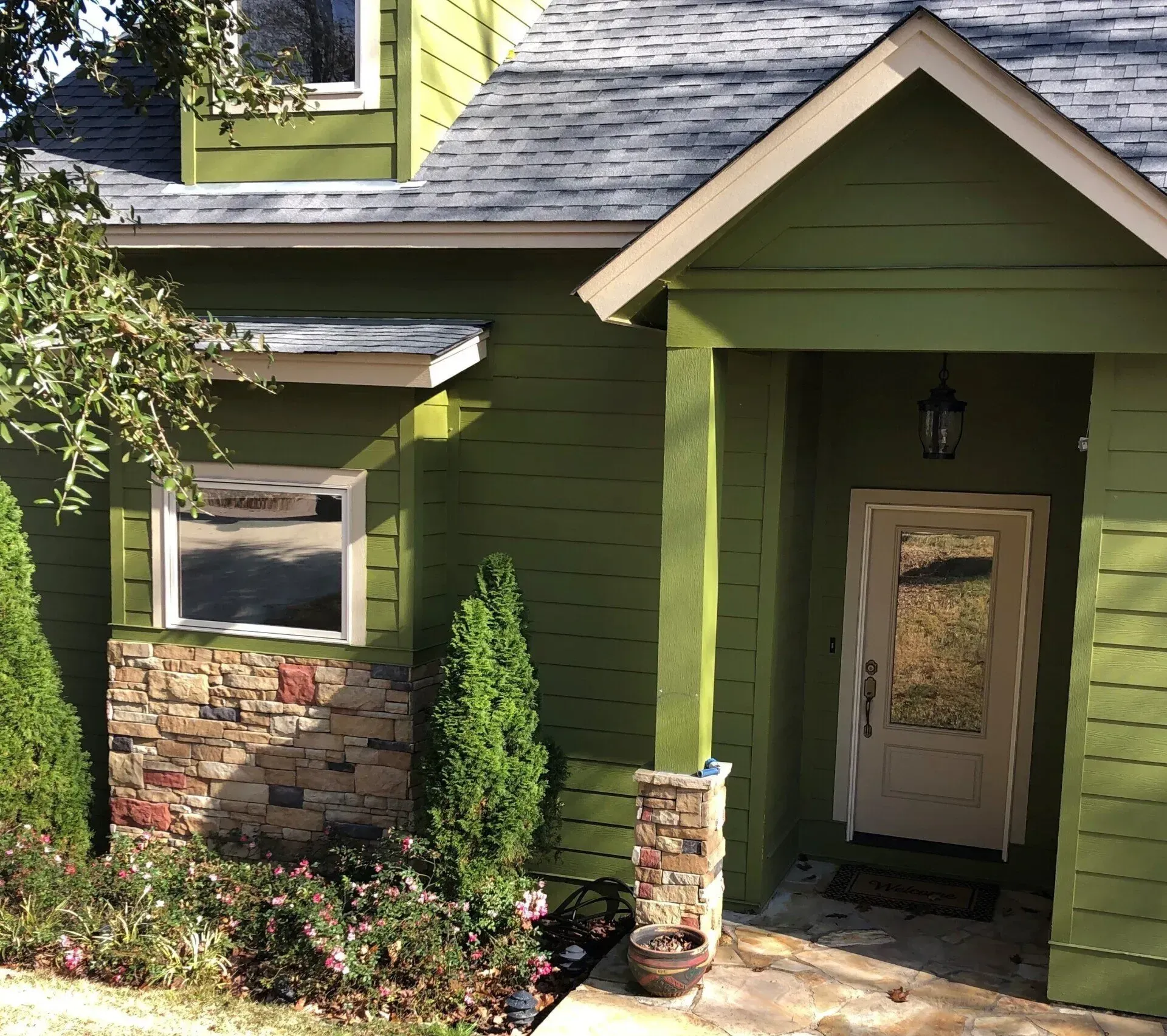 Green house entryway with stone accents, covered porch, and front door in sunlight