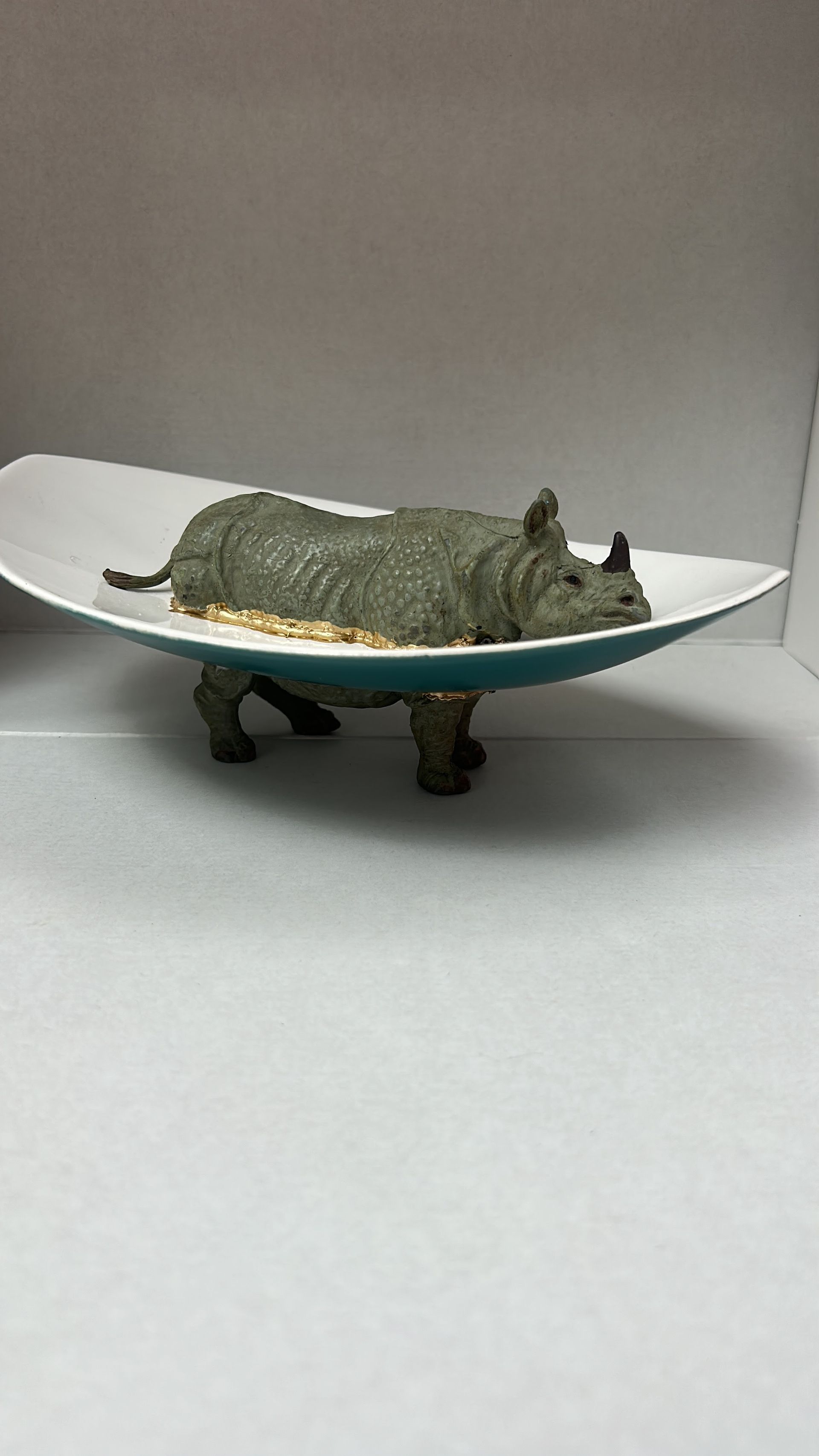 Klein, gestructureerd dierenfiguurtje op een wit, gebogen schaaltje, gezien tegen een grijze achtergrond.