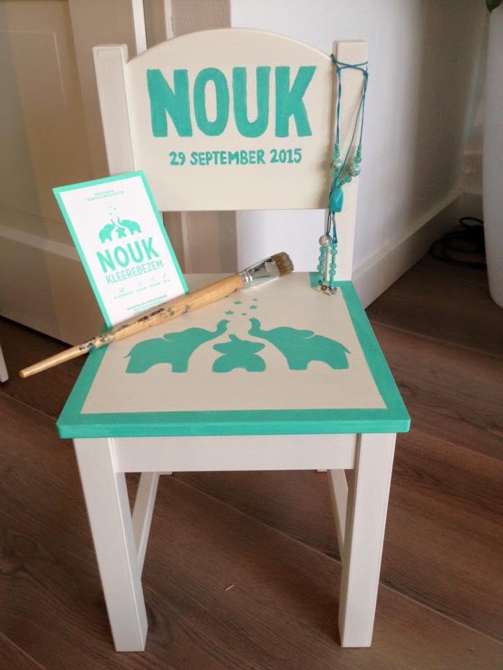 Witte stoel met turquoise bordje met ‘Nouk’ en bijpassend ingelijst aandenken op een houten vloer