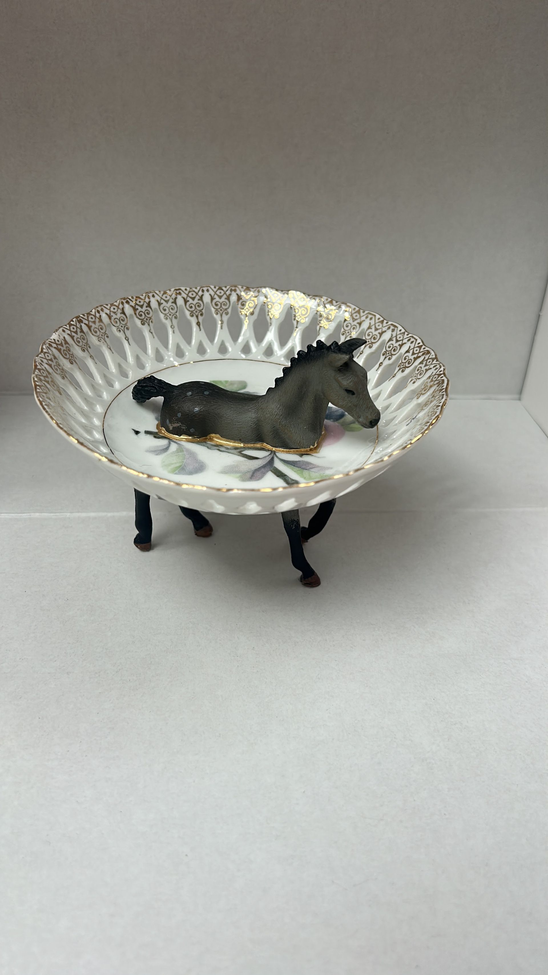 Klein zwart beeldje op een decoratieve schaal op een voetstuk met een goud-wit geschulpd patroon.