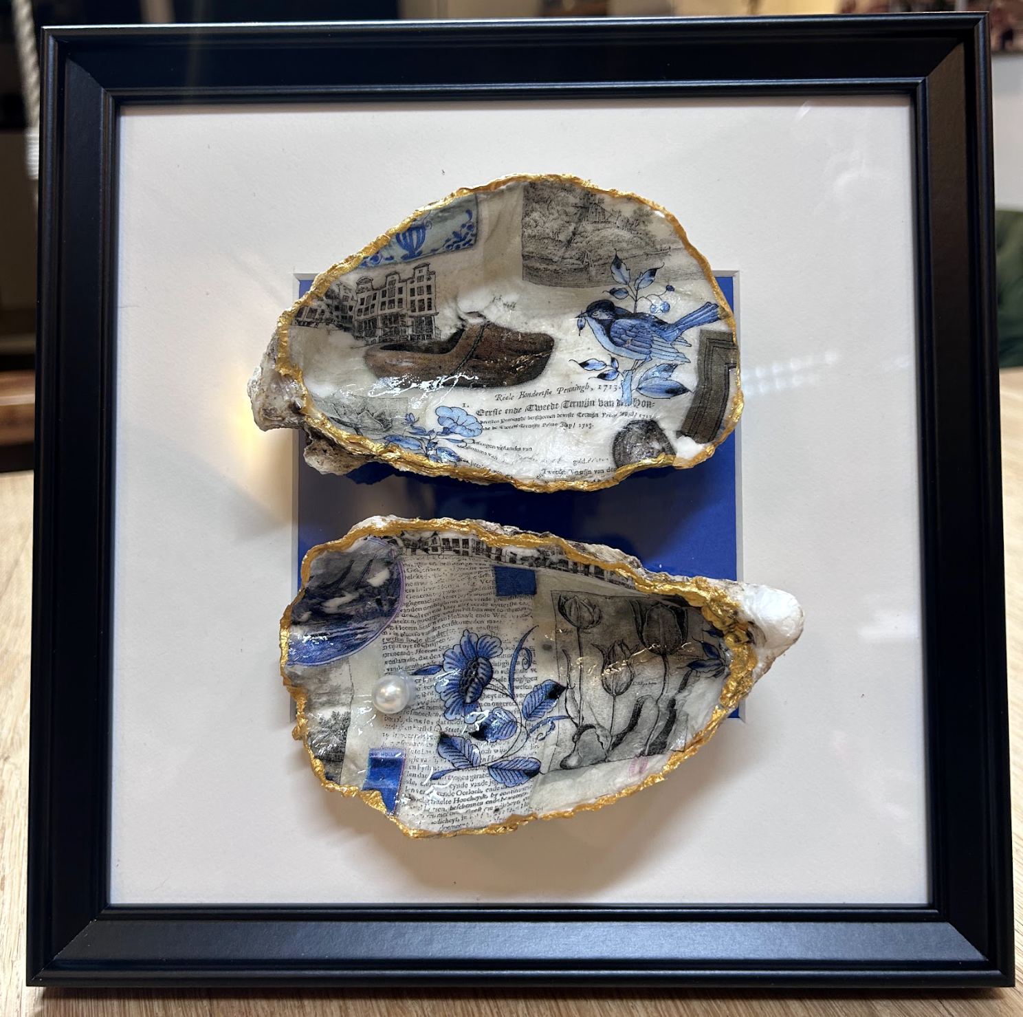 Ingelijst kunstwerk met twee schelpvormige keramische stukken, blauw en wit, gemonteerd op een witte achtergrond.