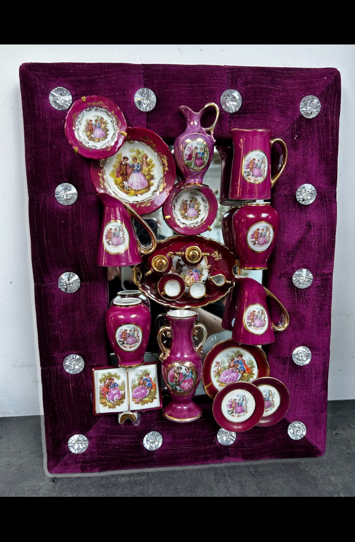 Bordeauxrood presentatiebord met decoratieve theekopjes, schotels en bordjes, gerangschikt in een bloemenpatroon.