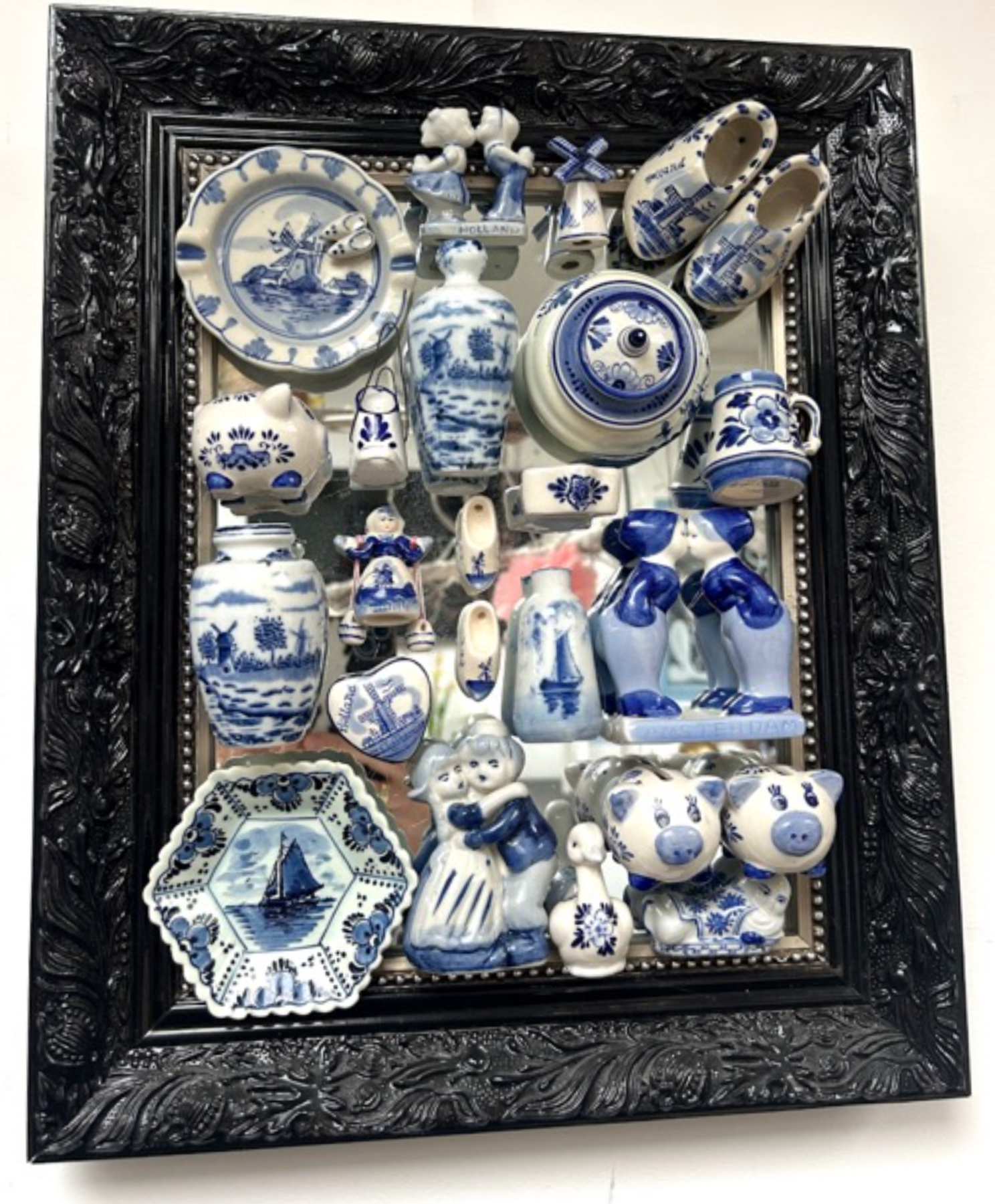 Een verzameling blauw-witte porseleinen theepotten en beeldjes, tentoongesteld in een vitrine met zwarte lijst.