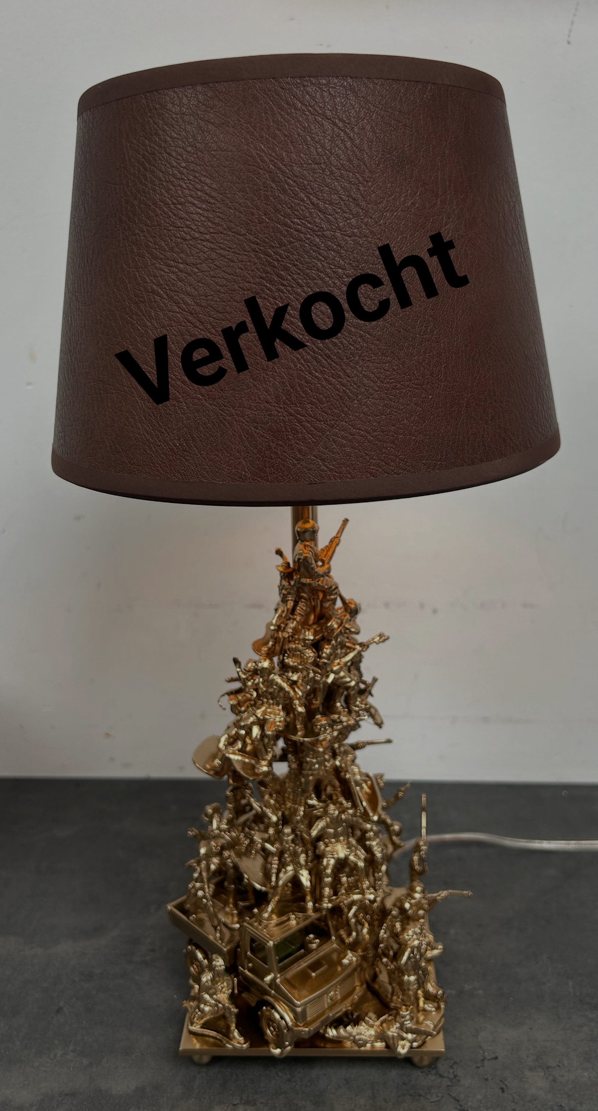 Bruine lamp met een goudkleurige, boomvormige voet en kap met het opschrift 