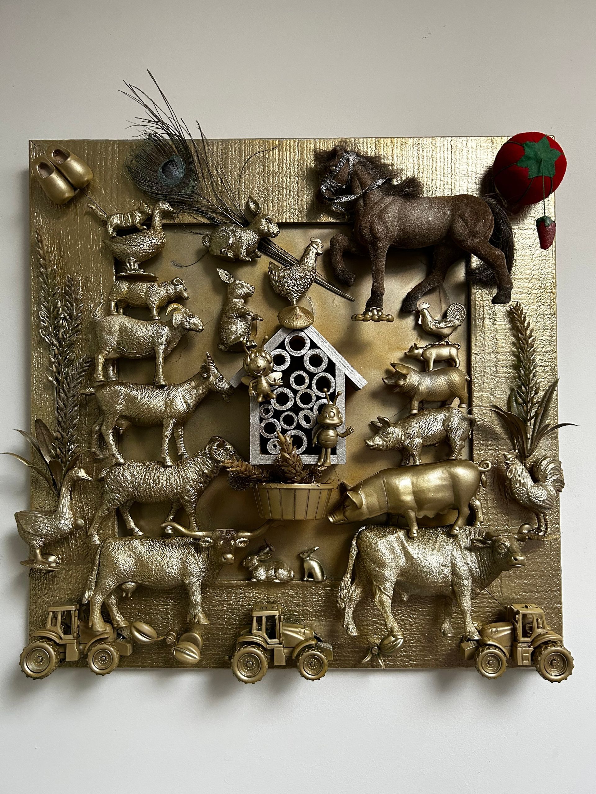 Goudkleurig decoratief reliëf van dieren, waaronder een paard, koe, hond en vogels, op een vierkante, gestructureerde plaat.