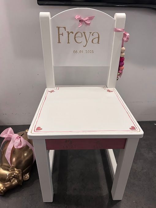 Witte kinderstoel met roze lint en ‘Freya’ op de rugleuning, naast een gouden ballonhond.