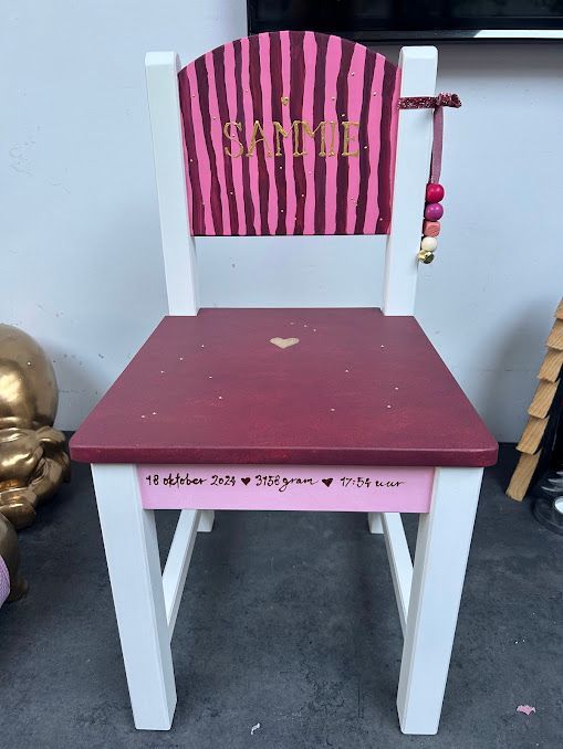 Rode stoel met witte poten en een roze gestreeunde rugleuning op een grijze vloer, geflankeerd door andere stoelen.