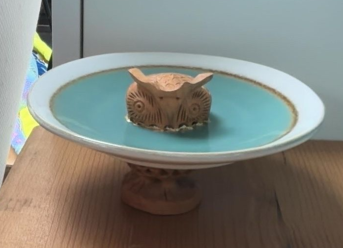 Keramische uilenfontein met turquoise water in een witte kom op een houten tafel.