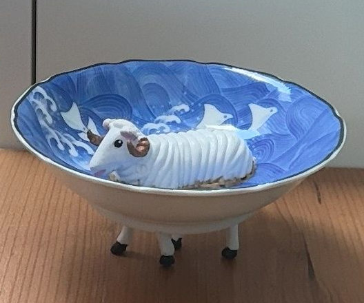 Een wit schaapje in een blauw, patroonvormig schaaltje op een houten ondergrond.