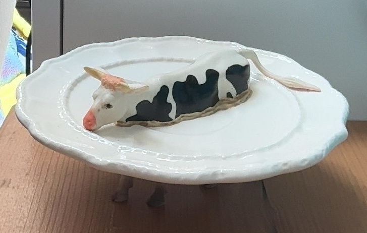 Klein zwart-wit kattenbeeldje op een wit bord, vastgehouden door een hand boven een houten tafel.