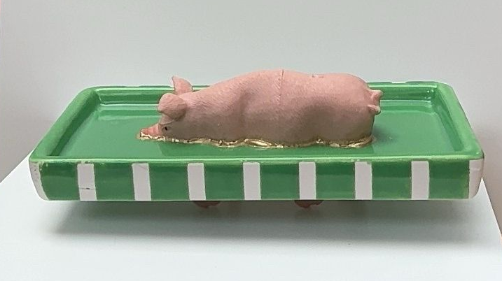 Roze speelgoedvarkentje op een groen dienblad met witte strepen