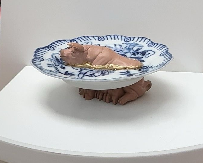 Een klein babyfiguurtje ligt in een blauw-wit gedecoreerde kom op een witte tafel.