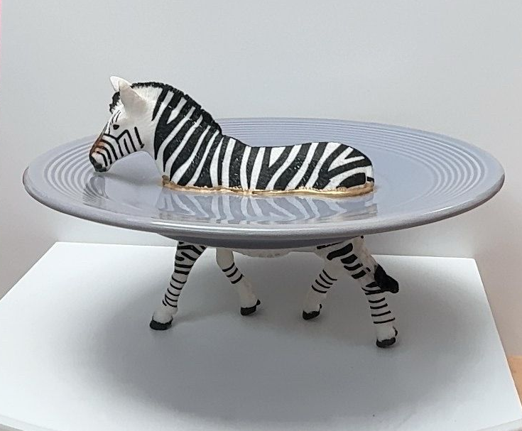 Een gestreept zebrafiguurtje dat een rond tafelblad ondersteunt, als een kleine tafel in de vorm van een dier.