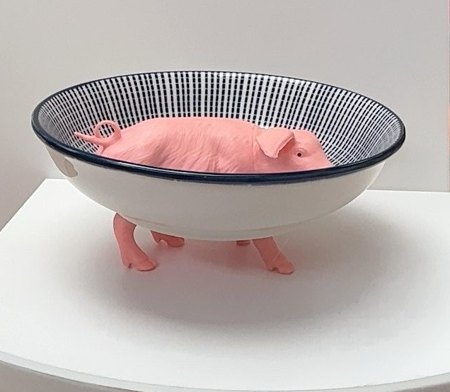 Roze, varkensvormig voorwerp in een witte kom op een ronde tafel.