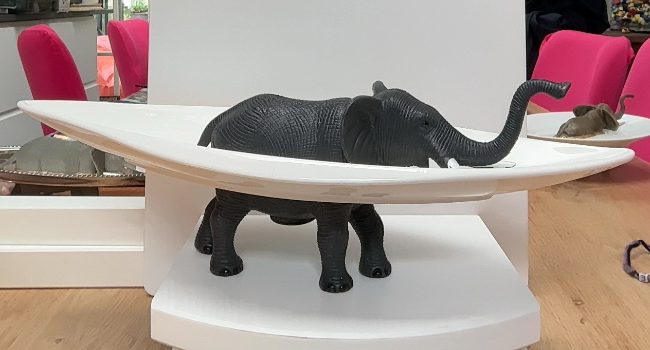 Een zwart olifantenbeeldje op een wit, draaibaar displayrek in een winkel of showroom.