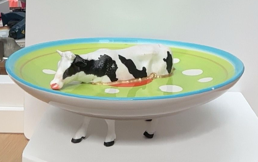 Een zwart-wit koeienfiguurtje dat op vier witte poten in een groene speelgoedkom ligt.