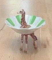 Een giraffefiguur staat in een witte kom met groene strepen op een houten ondergrond.