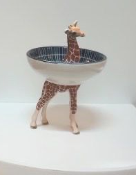 Een kom in de vorm van een giraffe op een witte ondergrond, met een blauw patroon op de bovenkant en giraffenpoten.