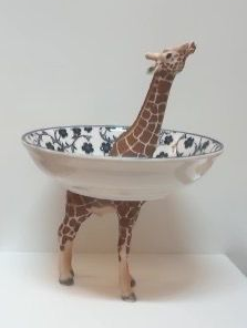 Giraffefiguur met een decoratieve kom rond zijn lichaam, op een effen witte achtergrond.
