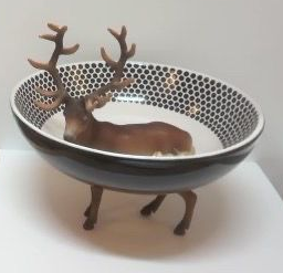 Klein hertenbeeldje in een witte kom met zwarte stippen aan de binnenkant, rustend op drie kleine pootjes.