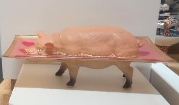 Een varken op een schaal, met de poten eronder zichtbaar, tentoongesteld op een witte standaard.