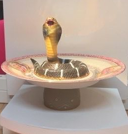 Een cobra die uit een decoratieve schaal op een sokkel tevoorschijn komt, wordt binnenshuis verlicht.